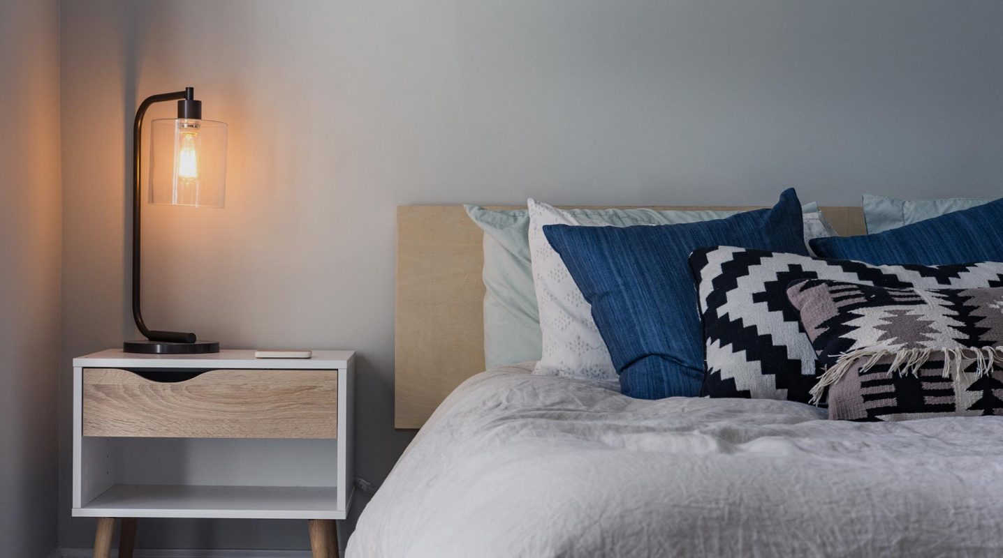 A stylish bedroom interior design in Ras Al Khaimah, featuring a cozy bed with cushions, a side table, and elegant decor.